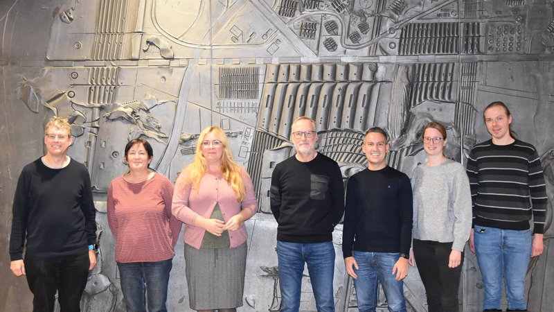 Die Bürgerjury steht vor der dunklen Wand des Magistratszimmers.