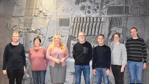 Die Bürgerjury steht vor der dunklen Wand des Magistratszimmers.