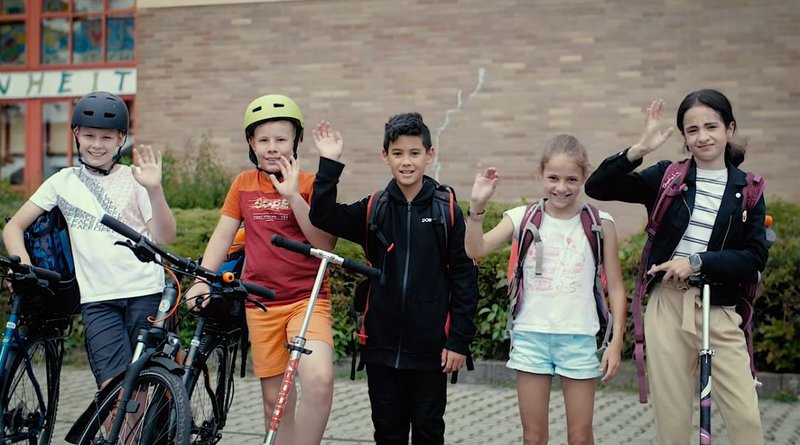 Schülerinnen und Schüler winken in die Kamera.