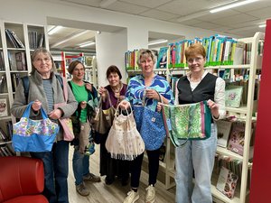 Fünf Frauen mittleren Altern stehen mit den bunten Taschen vor Bücherregalen