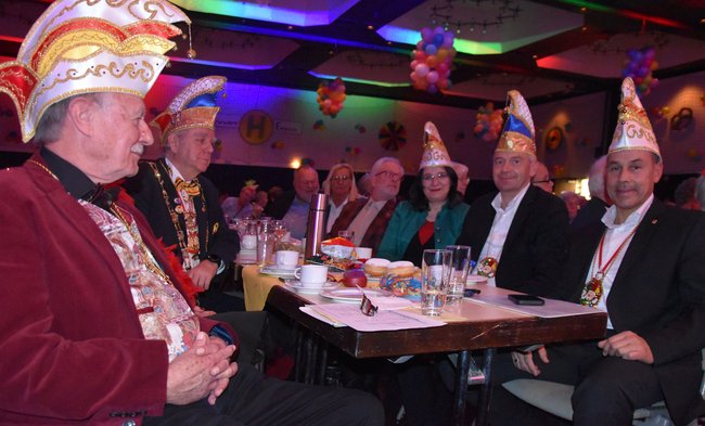 Landrat, Bürgermeister, Seniorendezernent und Erste Stadträtin sitzen mit Narrenkappen am Tisch.