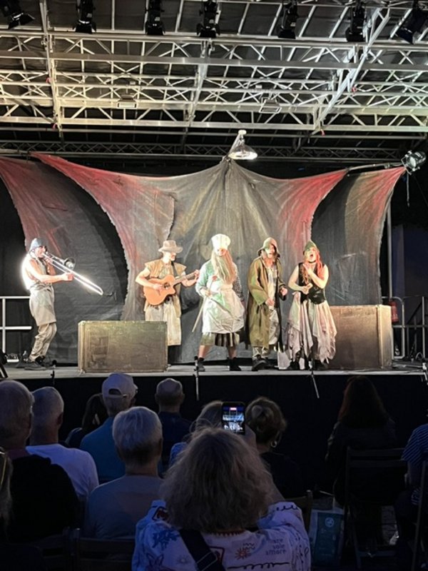 Fünf Schauspielerinnen udn Schauspieler auf der Bühne. Einer spielt Posaune, einer Gitarre.