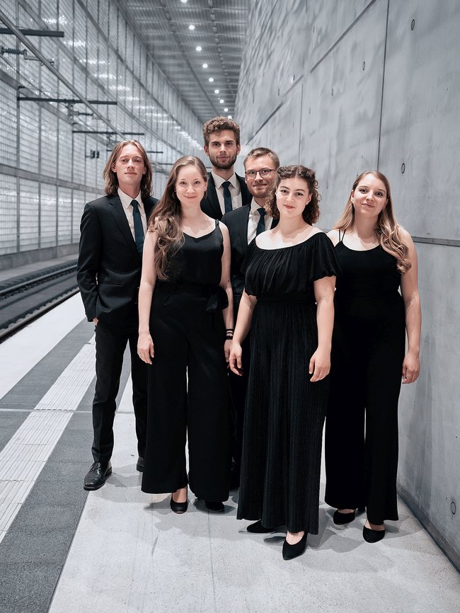 Das Ensemble voicemade in schwarzer Kleidung vor einer grauen Betonwand