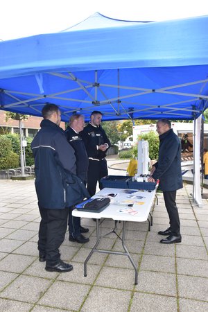 Bürgermeister Shaikh und die drei Polizisten stehen unter einem blauen Pavillon am Infostand.
