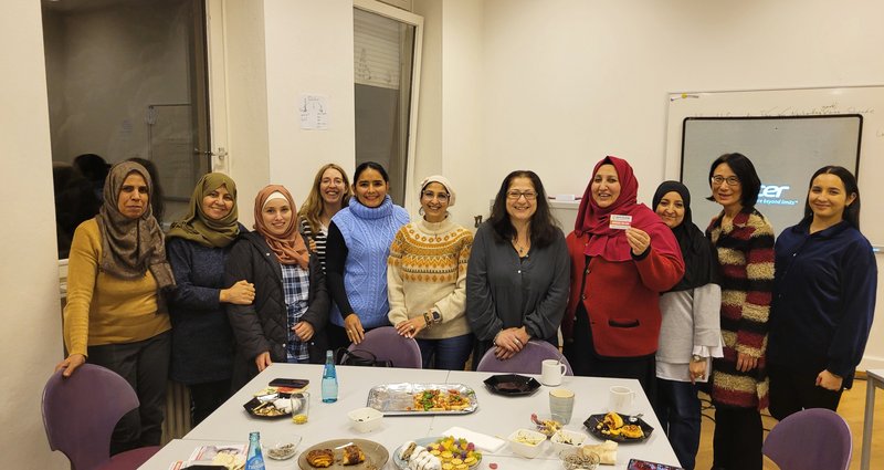 Elf Frauen stehen hinter einem Tisch, auf dem Teller stehen. In der Mitte steht Nil Esra Dağistan.
