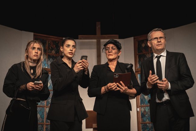 Ein Mann und vier Frauen, alle schwarz gekleidet, blicken ungläubig an der Kamera vorbei