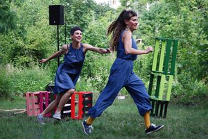 Zwei Frauen in blauen Overalls rennen durch einen Garten.