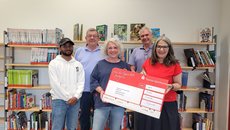 Mohammed Taj Alam, Lothar Baumgartl, Katrin Oberstedt, Michael Jersch und Bärbel Grade mit dem rot-weißen Spendenscheck vor einem Bücherregal in der Stadtbücherei.