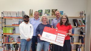 Mohammed Taj Alam, Lothar Baumgartl, Katrin Oberstedt, Michael Jersch und Bärbel Grade mit dem rot-weißen Spendenscheck vor einem Bücherregal in der Stadtbücherei.