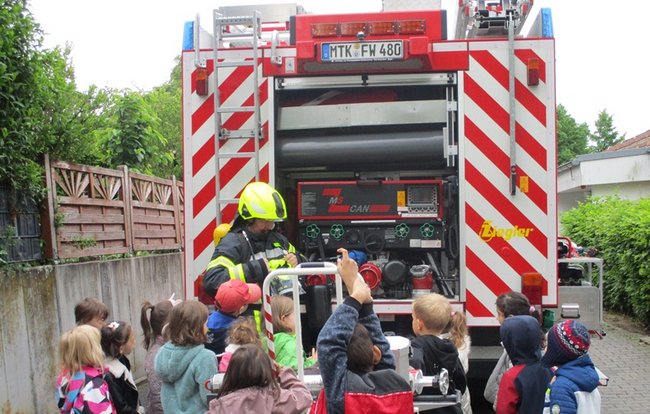 Eine Person in Schutzkleidung der Feuerwehr mit einer Kindergruppe vor einem Rettungswagen.