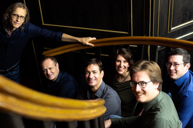 Die sechs Mitglieder von Singer Pur sitzen auf einer Holztreppe.