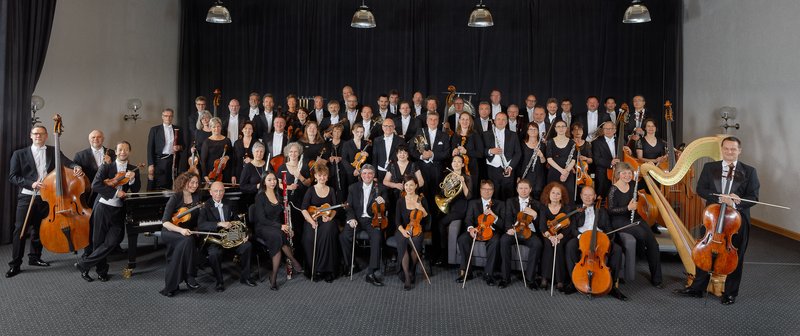 Das Orchester posiert dunkel gekleidet mit seinen Instrumenten für ein Gruppenfoto.