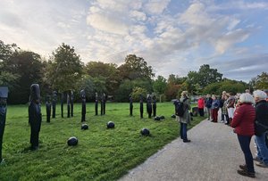 Die Gruppe der Kunstführung steht rechts, gegenüber von großen, schmalen Skulpturen und hört Ingrid Schlögel zu.