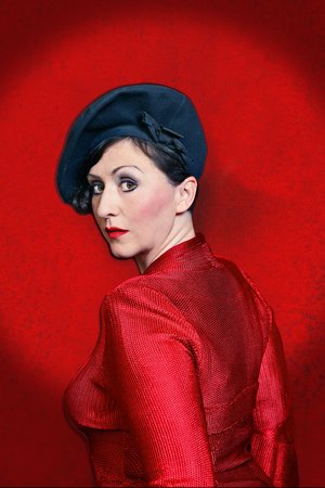 Evi Niessner mit schwarzem Hut und roter Kleidung vor rotem Hintergrund