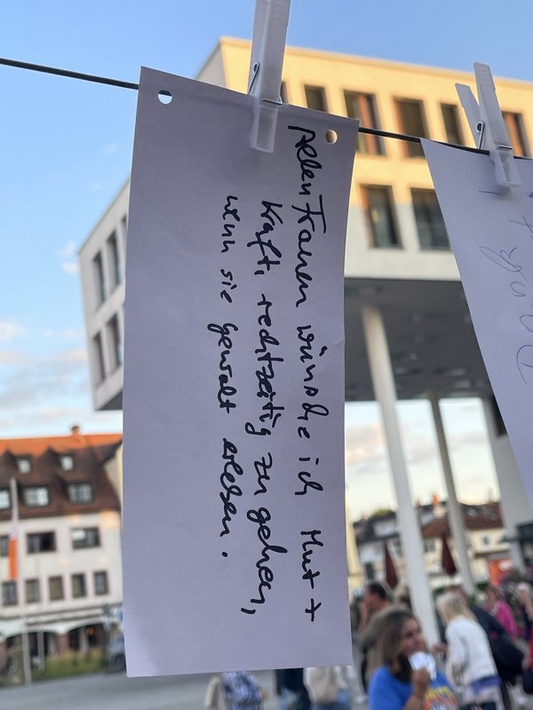 An einer Leine ist mit einer weißen Wäscheklammer ein Papierstreifen befestigt. Darauf hat jemand geschrieben: Allen Frauen wünsche ich Mut + Kraft, rechtzeitig zu gehen, wenn sie Gewalt erleben.
