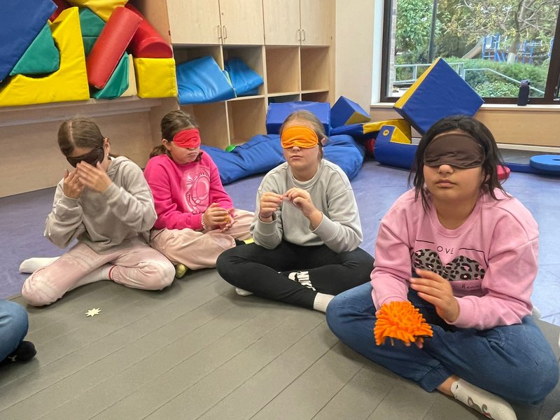 Vier Kinder sitzen auf dem Boden, tragen Augenbinden und ertasten Gegenstände.