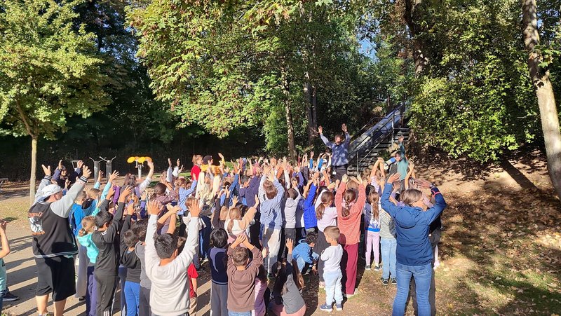Viele Kinder stehen im Park und halten jubeln die Hände in die Luft.