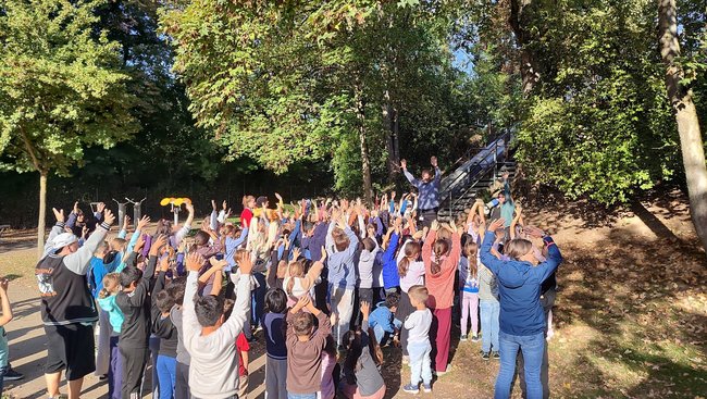 Viele Kinder stehen im Park und halten jubeln die Hände in die Luft.