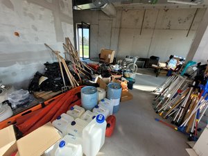 Man sieht einen Raum mit grauen Betonwänden, in dem viele Kisten mit Spenden, Kanister und Krücken stehen.