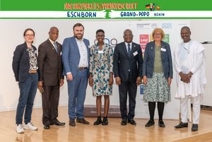 Vertreterinnen und Vertreter aus Eschborn und Grand-Popo posieren für ein Gruppenfoto. Über ihren Köpfen befindet sich ein Banner mit der Aufschrift "Nachhaltigkeitspartnerschaft Eschborn - Grand-Popo Bénin"
