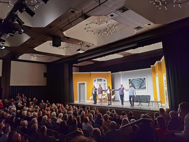 Fünf Schauspielerinnen und Schauspieler halten sich auf der Bühne an den Händen und verbeugen sich. Der Saal ist voll besetzt.