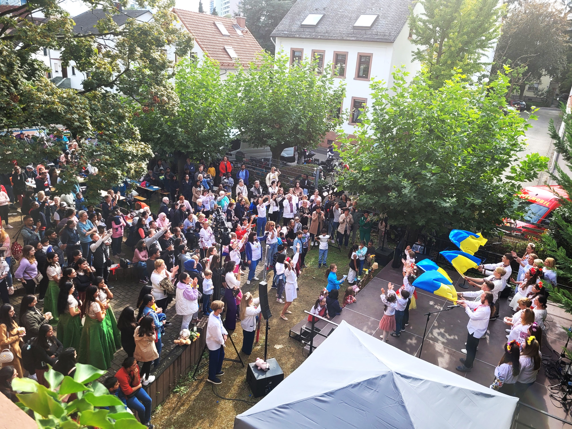 Blick aus der Vogelperspektive auf die Bühne, wo ukrainische Flagggen geschwenkt werden. Vor der Bühne stehen viele Menschen und sehen zu.