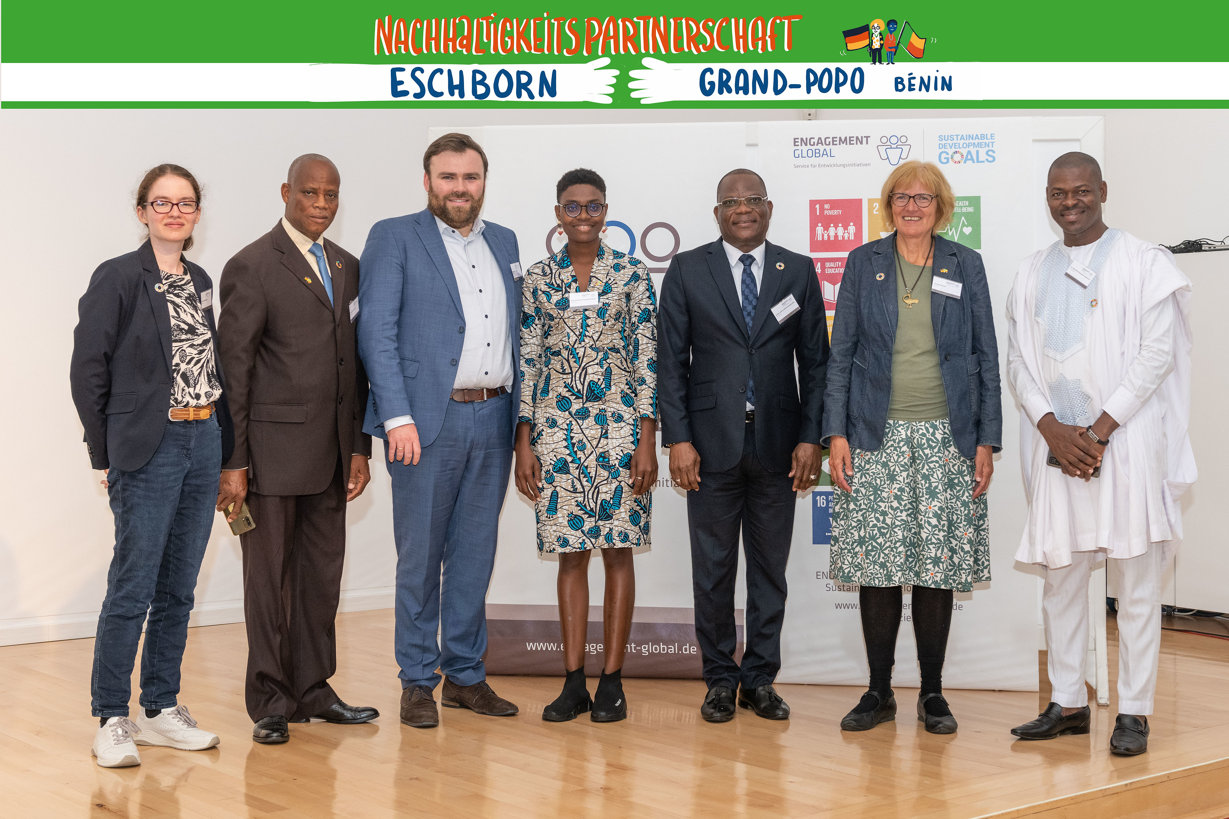 Vertreterinnen und Vertreter aus Eschborn und Grand-Popo posieren für ein Gruppenfoto. Über ihren Köpfen befindet sich ein Banner mit der Aufschrift "Nachhaltigkeitspartnerschaft Eschborn - Grand-Popo Bénin"