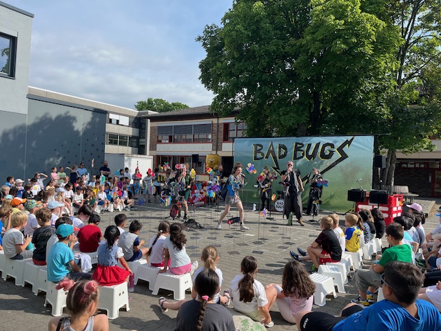 Eine Gruppe Kinder sitzt auf dem Schulhof und schaut dem Theaterstück zu.