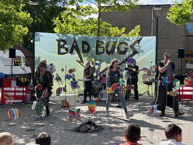 Musikerinnen und Musiker spielen vor einem Banner mit dem Aufdruck "Bad Bugs".