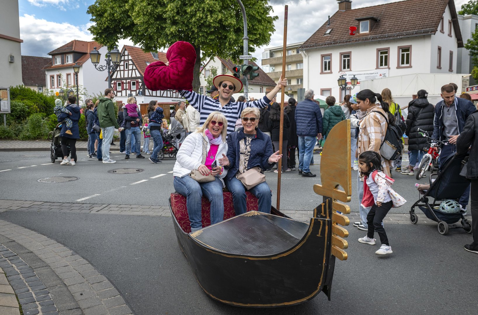 Zwei Frauen sitzen fröhlich in einer Gondel auf der Unterortstraße. Der Gondoliere hält ein rotes Stoffherz hoch.