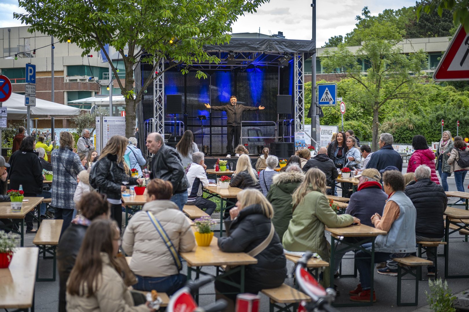 Auf braunen Bierbänken sitzen die Besucherinnen und Besucher an Tischen vor der blau beleuchteten Bühne in der Unterortstraße.